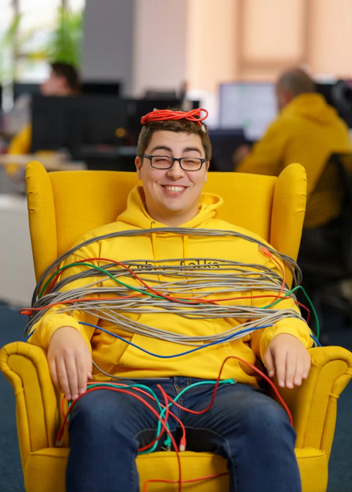 Persoană legată cu cabluri, zâmbind pe scaun galben.