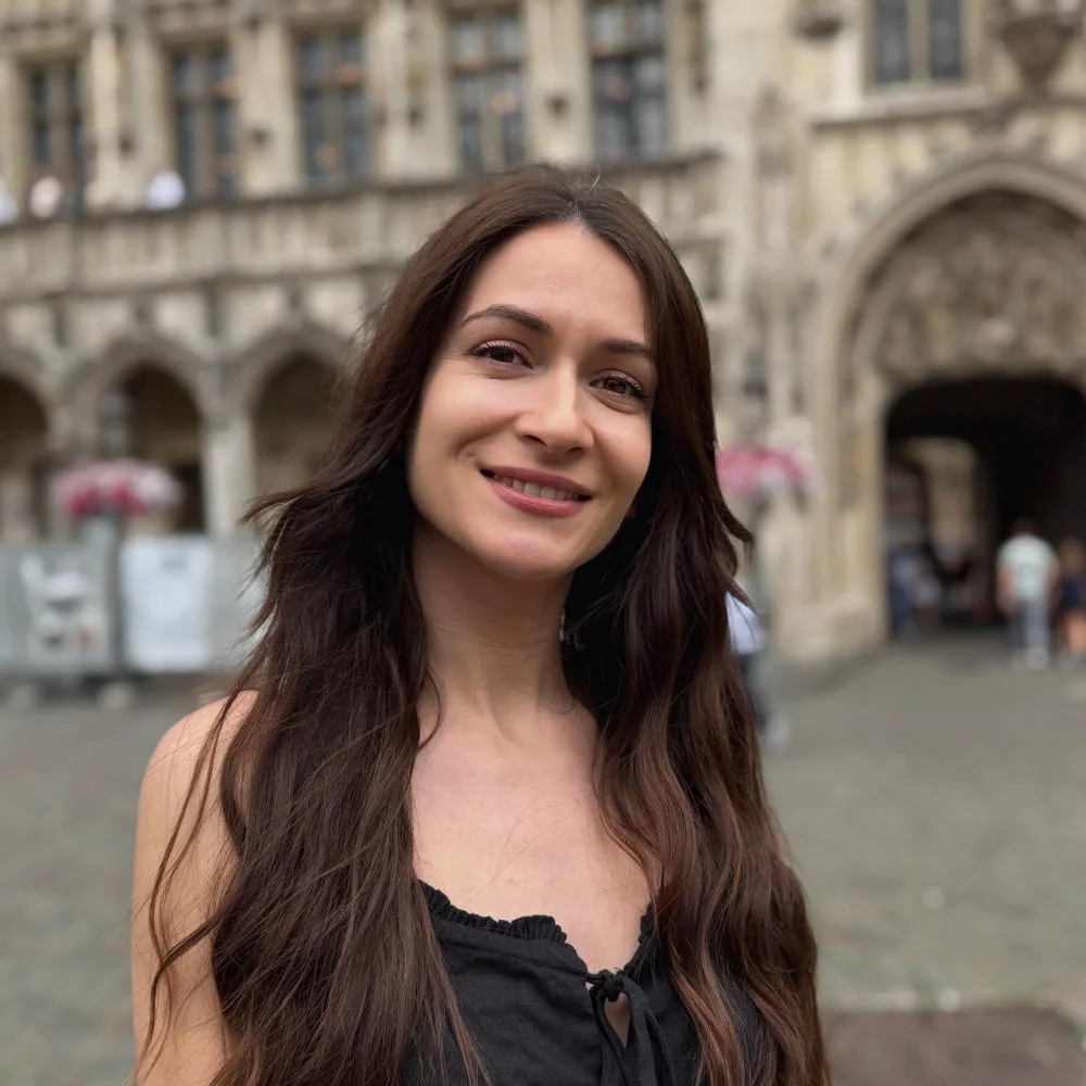 Femeie zâmbitoare în fața unei clădiri istorice.